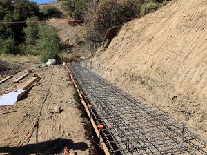 Steel rebar grid laid in a trench on a hillside, prepared for concrete foundation at a construction site.