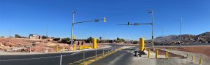 A clear blue sky over an empty desert road with traffic lights and rocky terrain on both sides.