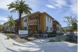Modern two-story apartment building with palm trees, greenery, and a sign reading 200 in front.