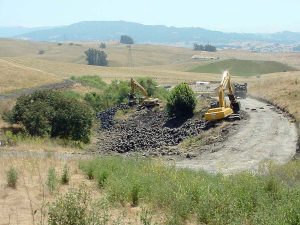 Excavators clearing tires from a rural, hilly landscape with fields and distant mountains.