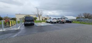 Four cars parked in a small parking lot next to a beige building under a cloudy sky.
