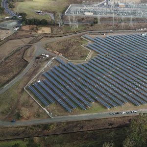 Aerial view of a large solar panel farm near power lines and a substation in a rural area.