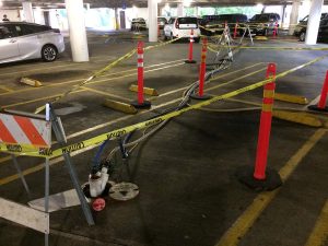 Parking lot with caution tape, cones, and hoses blocking several spaces due to maintenance work.