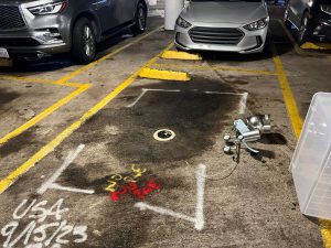 A scorched parking spot with debris, surrounded by cars, marked with white and yellow paint, dated 9/13/23.