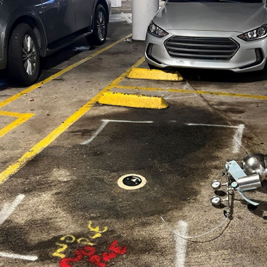 A car is crashed into a parking barrier, with debris and spilled fluid on the ground in a parking garage.