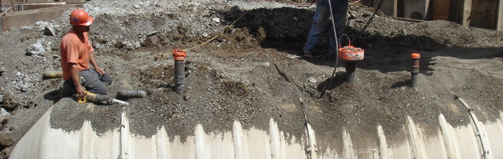Two construction workers install and cover a large underground storage tank with gravel and soil.