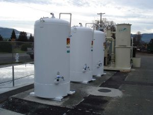 Three large white industrial storage tanks are positioned outdoors on a concrete surface near a fenced area.