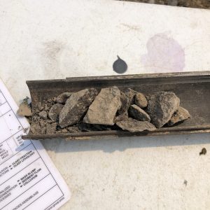 Broken rock fragments in a metal tray next to a partially visible form with printed text.
