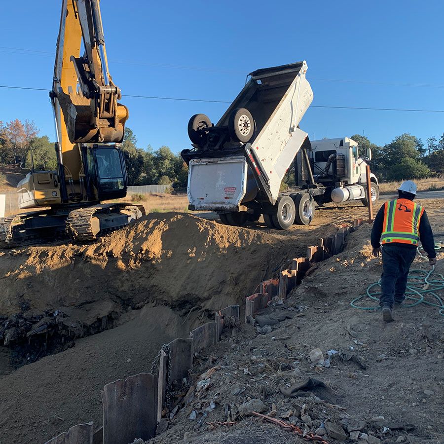 A dump truck tips backward near an excavation site as a worker in a safety vest approaches.