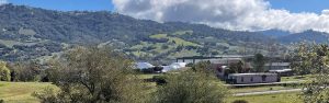 Green hills under a partly cloudy sky with buildings and trees in the foreground.
