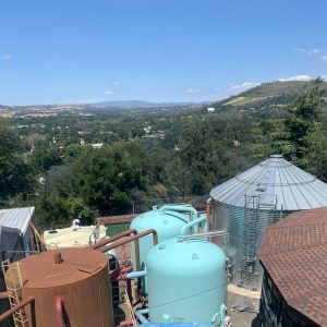 Large storage tanks and silos in the foreground with a scenic hilly landscape and town in the background.